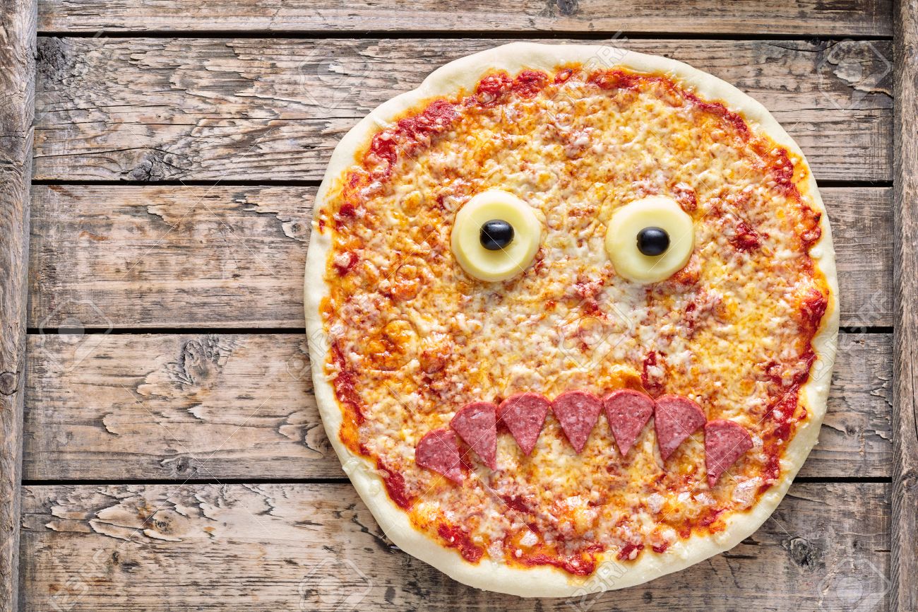 Halloween scary food funny monster face pizza horror snack with mozzarella and sausage on vintage wooden table background. Traditional creative homemade holiday celebration party decoration